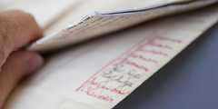 A hand folding a folded piece of paper with illegible red and black writing on it.