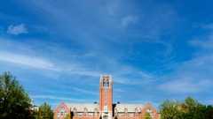 View of a large red brick campus building at John Carroll University with a central clock tower under a blue sky.