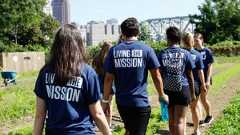 A group of people wearing matching blue shirts that say Living the Mission walk along a dirt path in a garden.