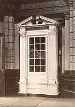Tall, architectural case with column-like details, carved moulding, and window.