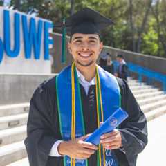 Smiling student wearing graduation cap & gown at the UWF entrance plaza