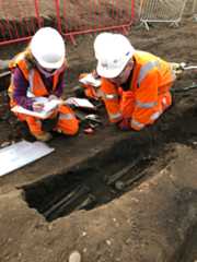 Archaeologists and osteologists examining a burial in an earth-cut grave.