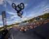 A man is seen upside down on his BMX bike after hitting a half pipe jump. There is a crowd of people behind him in the background an a FISE World flag.