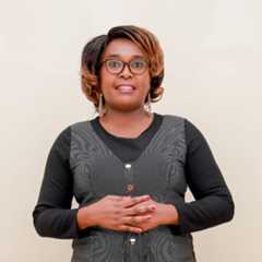 A person standing in front of a white wall with hands clasped