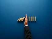 Businessperson stopping falling dominos with their hand.