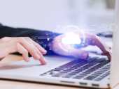 Person's hands typing on a laptop with a glowing cloud computing icon hovering over the keyboard.