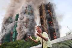 A man reacts, as smoke rises while flames engulf bamboo scaffolding across multiple buildings at Wang Fuk Court housing estate, in Tai Po