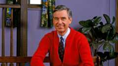 Mister Rogers wearing a red sweater and black tie