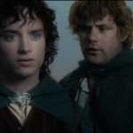 Frodo- a dark-haired young man in a green cloak- stands with his friend Sam in front of a cloudy sky.