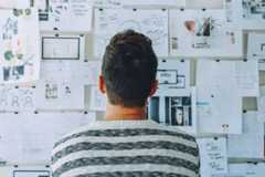 Image of man facing away from camera toward wall covered in notes, diagrams and images.