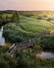 Wandelaar steekt houten hangbrug over in groen natuurgebied bij zonsondergang in Brabant.