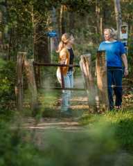 Twee vrouwen wandelen door een houten klaphek op een bospad in Brabant.