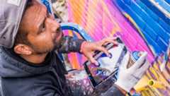 Over ons: Kunstenaar sprayt kleurrijke muurschildering met tablet in hand.