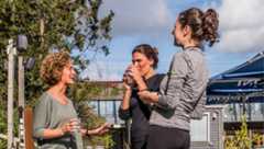 Drie vrouwen praten en drinken water tijdens buitenbijeenkomst op zonnige dag.