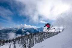 Downhill skier gets air off snowy mountain ridge