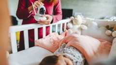 woman adjusting a baby monitor near bed of a sleeping child