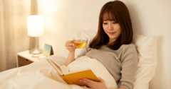 ベッドに座り、毛布にくるまりながら読書を楽しむ女性。