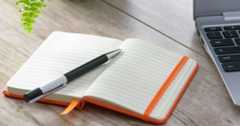 デスクの上にノートとペン、ラップトップが置かれている