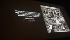 On a black theater screen white text reads: "I could see and feel that there were other voices out there and there were other stories to be told...but they weren't being given a chance." -- Robert Redford. Next to the quote is a black and white photo of a group of people, including Robert Redford, talking outside of a wood cabin with the sign "Sundance Institute" over the threshold.