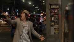 A man wearing a beige blazer, fedora and button-up clutches an orange extension cord and raises it in the air. He makes a shocked facial expression.