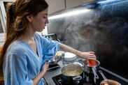 Home cook calculates exact time to cook pasta for it to be al dente Woman cooking pasta sauce in modern kitchen