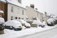 Parked cars and houses on the High Street covered in thick snow after blizzard.