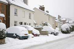 Parked cars and houses on the High Street covered in thick snow after blizzard.