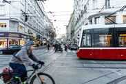 Vienna, Austria - 15 December, 2025: Busy street scene in Vienna, Austria. A cyclist rides past a red tram. People walk along the sidewalk. Urban arch