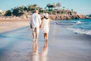Romantic senior couple walking barefoot on the seashore at sunset enjoying vacation and retirement, 