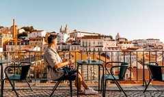 Man drinking coffee at a sidewalk cafe with view of Lisbon cityscape on a sunny summer day, Portugal