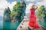 A famous cliffs and islands of Thailand to advertise tours. A woman in a dress on a Thai longtail boat looks at the Three Rocks nature panorama on Cheo Lan Lake in Khao Sok Park.