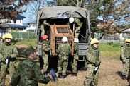 In this photo provided by the Japan Self-Defense Forces Akita Camp, Self-Defense forces personnel unload a bear cage from a mili
