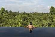 tourist relaxing in infinity pool overlooking forested area in Cambodia