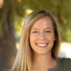 Haley miller smiling outdoors with blurred trees and sunlight.
