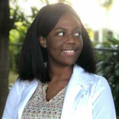 Woman named shennel smiling outdoors in a white coat.