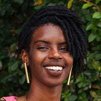 Woman with natural hair and gold earrings smiles in foliage.