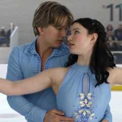 Cale Ambrozic as Brayden Elliot and Madelyn Keys as Adriana Russo wearing matching blue uniforms figure skating together with a crowd in the bleachers in a still from finding her edge