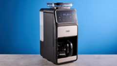 the gevi 10-cup drip coffee maker with grinder photographed against a blue background, showing the glass carafe, water tank, touch screen, and accessories including plastic filter