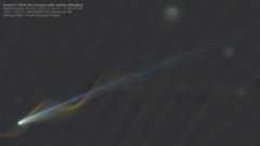 A comet is pictured with a bright nucleus in the lower right of an image against the blackness of space, with a long tail extending diagonally to the upper right of the shot. A spiral or light is pictured, appearing to wrap around the comet and its tail, created by the trail of a passing meteor.