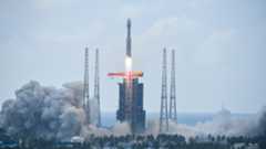 A rocket launches from a large launchpad with smoke billowing all around