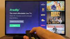 A smart TV with the Frndly TV app open and an outstretched hand pointing a remote at the screen