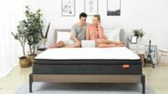 A couple sits on the SweetNight Twilight Mattress in a sunny bedroom