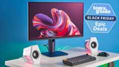 An image of an Alienware Monitor as part of a slick gaming set up, with a blue background and green/pink RGB lighting visible throughout.