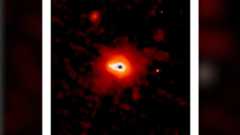 A glowing dark dot surrounding by blobs of white, orange and red light sits on a dark background