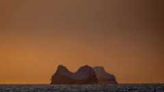 a view of a glacier in the ocean with an orange sky behind it