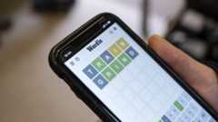 Wordle is open on a phone held in a hand. TRAIN and GRIND have been played, with the RIN in GRIND all green.