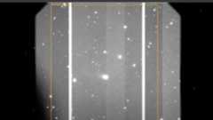 A gray scale image showing various white dots of stars and comets with a large smudge in the middle which is the interstellar comet 3I/ATLAS