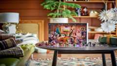 A festive workshop is displayed behind the various figures and mini builds included in the advent calendar, all displayed on a table in a living room.