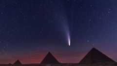 A bright comet streaking down a purple starry sky over the pyramids of Giza.