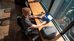 Person using a Dell Plus laptop sat at a desk in front of the window of a skyscraper